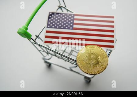 Kleiner Warenkorb mit goldenem Bitcoin und Flagge der Vereinigten Staaten von Amerika USA auf dem Tisch. Stockfoto