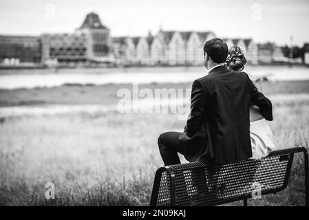 Eine Graustufenaufnahme eines Paares, das auf einer Bank am Fluss sitzt. Stockfoto