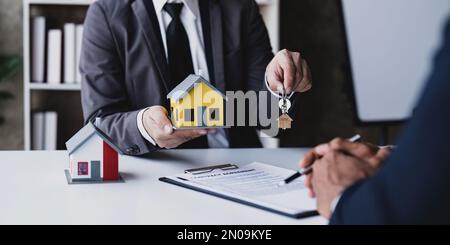 Der Immobilienmakler hat die Schlüssel und das Modellhaus wird den Kunden ausgehändigt, Immobilienkonzept. Stockfoto