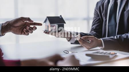 Immobilienmakler gibt den Schlüssel für lächelnde Kunden. Das glückliche Paar unterschreibt Papiere und nimmt den Schlüssel für ein neues Zuhause mit. Konzept einer jungen Familie, die Träume wahr werden lässt Stockfoto
