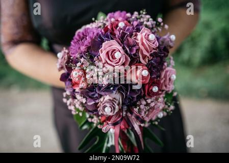 Nahaufnahme einer Brautjungfer mit einem lila, rosa Blumenstrauß mit Perlen Stockfoto
