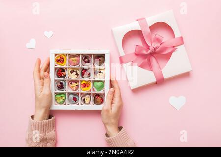 Weibliche Hände mit köstlichen Süßigkeiten in der Schachtel auf farbigem Hintergrund. Stockfoto