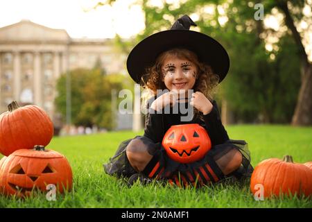 Süßes kleines Mädchen mit Kürbis-Süßigkeiten-Eimer in Halloween-Kostüm im Park Stockfoto