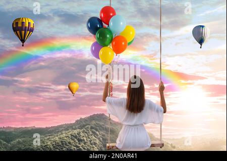 Traumwelt. Junge Frau mit hellen Ballons, die schwingen, Berge unter dem Himmel bei Sonnenuntergang im Hintergrund Stockfoto