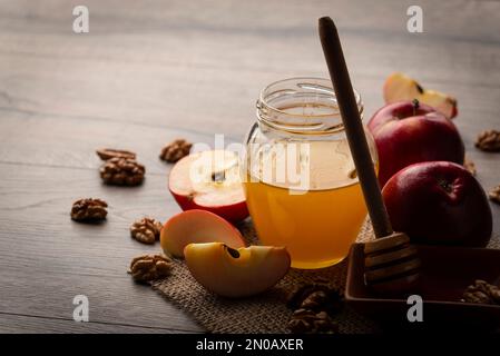 Einmachglas mit Honig Honig Dipper rote Äpfel und Walnüsse auf Küchentisch Stockfoto