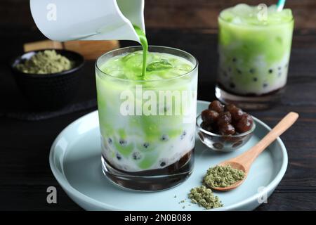 Grünes Matcha in Glas mit Milchblasentee auf schwarzem Holztisch, Nahaufnahme Stockfoto