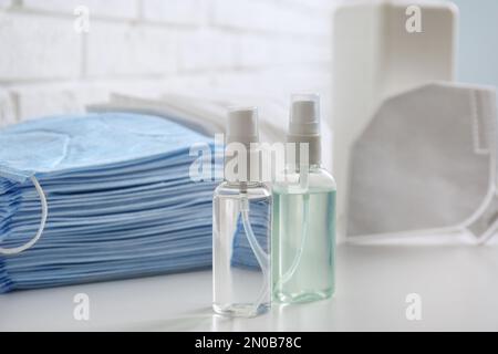 Handdesinfektionsmittel und Atemschutzmasken auf weißem Tisch in Innenräumen. Wichtige Schutzmaßnahmen während der COVID-19-Pandemie Stockfoto