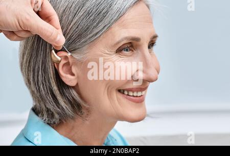 Nahaufnahme des Hörgerätes in der Nähe des weiblichen Seniorohres an der audiologischen Klinik. Hörlösungen, Hör-BTE-Hilfsmittel Stockfoto