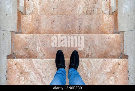 Männerfüße auf den Stufen. Ein Mann in Jeans und schwarzen Schuhen auf der Marmortreppe. Stockfoto