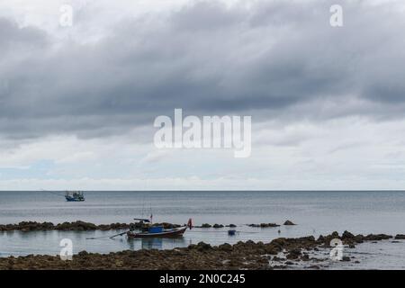 Zwei thailändische Fischerboote auf dem Meer, neben einem felsigen Strand. Wolkiger Himmel mit Kopierraum. Stockfoto