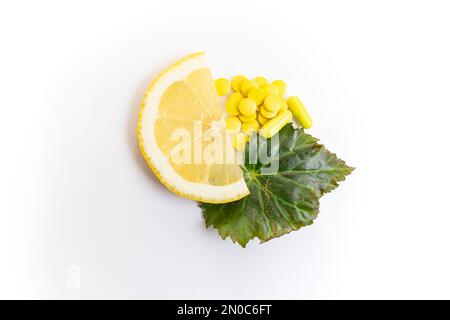 Eine halbe Zitronenscheibe neben gelben Pillen und Kapseln und ein grünes Blatt isoliert auf weißem Hintergrund Stockfoto