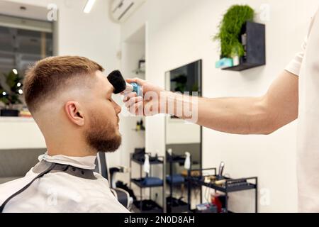 Friseurin, der gutaussehenden Mann im Friseursalon bedient. Stockfoto