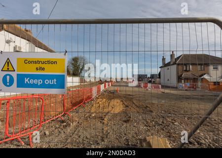 Rochford, Großbritannien. Februar 2023. Eine umzäunte Baustelle in einer Wohnstraße in Rochford, gekennzeichnet durch rote Sicherheitsbarrieren und ein markantes Warnschild mit der Aufschrift „Baustelle – halten Sie sich fern“. Das Gelände wird anscheinend einer Bodenvorbereitung unterzogen, wobei Häuser an beiden Seiten flankieren. Demonstranten von Save Holt Farm Oak Tree protestieren, um eine 100 Jahre alte Eiche zu retten. Der Baum wird voraussichtlich bis April 2023 gefällt. Penelope Barritt/Alamy Live News Stockfoto