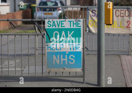 Rochford, Großbritannien. Februar 2023. Ein handgefertigtes Schild mit der Aufschrift „SAVE THE OAK / HELP THE NHS“, das an den Geländern in Rochford angebracht ist. Sichtbare Straßenszene umfasst geparkte Autos und zusätzliche Banner. Teil einer lokalen Demonstration, die sich für den Umweltschutz und die öffentliche Gesundheit einsetzt. Demonstranten von Save Holt Farm Oak Tree protestieren, um eine 100 Jahre alte Eiche zu retten. Der Baum wird voraussichtlich bis April 2023 gefällt. Penelope Barritt/Alamy Live News Stockfoto