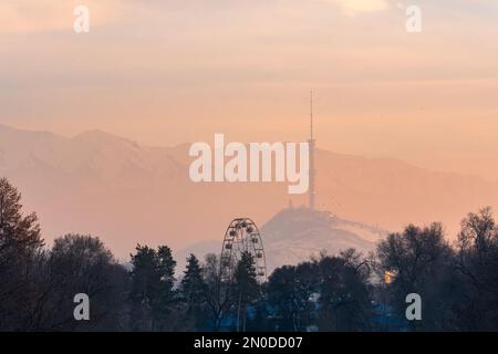 Blick auf den Sonnenuntergang im Winter vom Stadtpark zum Koktobe-Berg mit Fernsehturm in Almaty, Kasachstan Stockfoto