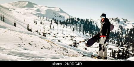 Snowboarder Mann mit Seitenansicht tragen schwarze Anzug Brille Maske Hut Ski gepolsterte Jacke Do Sieger Gesture feiern isoliert oben. Hintergrund Winter extreme sp Stockfoto