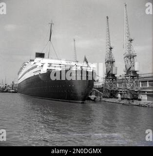 1950er, historisch, RMS Queen Elizabeth, vom Heck aus gesehen, das in den Docks in Southampton, Hampshire, England, Großbritannien, festgemacht ist. Das luxuriöse Seeschiff wird von der Cunard Line betrieben und segelte wöchentlich von Southampton, England, nach New York, USA, über Cherbourg in Frankreich. Erbaut von John Brown & Co auf dem Clyde in Schottland, wurde sie zu Ehren von Königin Elizabeth, später Königin Mutter, benannt. Als sie 1938 gestartet wurde, war sie das größte Passagierschiff, das je gebaut wurde, bis 1994. Stockfoto