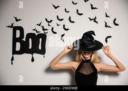 Eine Frau mit Hexenhut, die an der weißen Wand posiert, dekoriert für Halloween Stockfoto