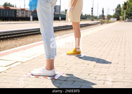 Leute, die auf festgeklebten Bodenmarkierungen für soziale Distanz am Bahnhof stehen, schließen. Coronavirus-Pandemie Stockfoto