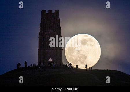 Glastonbury, Somerset, Großbritannien. 5. Februar 2023 Wetter in Großbritannien. Der Vollmond erhebt sich hinter dem St. Michael's Tower auf dem Glastonbury Tor in Somerset, während sich eine Menschenmenge auf dem Hügel versammelt, um zu beobachten. Bildnachweis: Graham Hunt/Alamy Live News Stockfoto