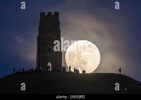 Glastonbury, Somerset, Großbritannien. 5. Februar 2023 Wetter in Großbritannien. Der Vollmond erhebt sich hinter dem St. Michael's Tower auf dem Glastonbury Tor in Somerset, während sich eine Menschenmenge auf dem Hügel versammelt, um zu beobachten. Bildnachweis: Graham Hunt/Alamy Live News Stockfoto