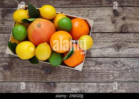 Mischung aus Zitrusfrüchten, Orangen, Grapefruit, Zitronen und Limetten mit Blättern im Karton auf Holzhintergrund, Draufsicht. Foto von oben. Stockfoto