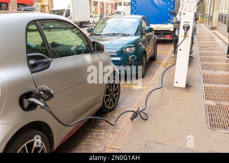 Aufladen eines kleinen grauen und grünen Elektroautos auf einer Straße der Stadt Stockfoto