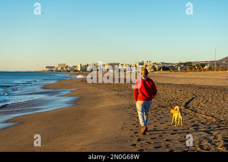 Mann mit Hund, der bei Sonnenaufgang über dem Mittelmeer an der Küste spaziert, Costa del Sol, Malaga, Spanien Stockfoto