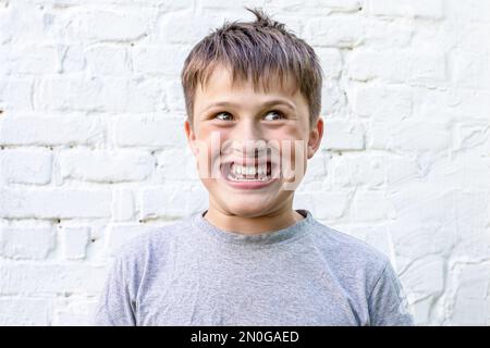 Ich grinste das Kind an. Der Junge lächelt bei 32 Zähnen. Rocky übertreibendes Kind. Komisches Gesicht bei einem Teenager. Die Gefühle der Kinder Stockfoto