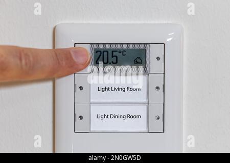 Mann, der die Temperatur an einem Thermostat reguliert, reduziert die Temperatur in der Wohnung in der globalen Energiekrise Stockfoto