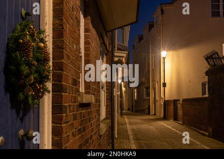 Portsmouth, England, 1. 2022. Dezember. Ruhige, alte Kopfsteinpflasterstraße, die nachts gemacht wurde, mit einem Weihnachtskranz, der an einer Tür im Vordergrund hing. Stockfoto