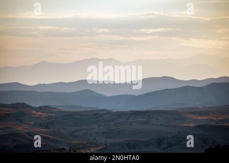 Die sanften Hügel und die majestätischen Bergketten sind in warmen Farbtönen der untergehenden Sonne beleuchtet und schaffen eine atemberaubende Landschaft von mehrschichtiger Schönheit. Stockfoto