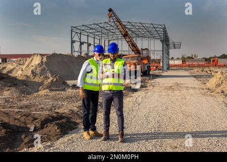 Zwei Ingenieure mit Helmen und Westen, die per Fernbedienung mit der Drohne arbeiten. Technologische Innovationen in der Bauindustrie Stockfoto