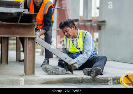 Der Ingenieur hat einen Unfall, bei dem bei der Arbeit Stahl auf sein Bein fällt und schwere Beinverletzungen verursacht. Und holen Sie sich die Hilfe von Kollegen in dem Bereich, in dem sich die Konstruktion befindet Stockfoto