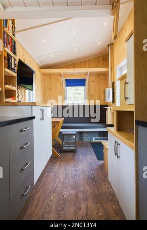 Brauner Kiefernholzboden und Blick auf die Küchenablagen, graue und weiße Melaminschränke und den Hauptsitzbereich im Hintergrund von der Badezimmertür. Stockfoto