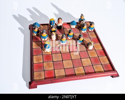 Ein handgemachtes Schachset aus Ecuador mit bunten Stücken auf dem Spielbrett mit weißem Hintergrund. Stockfoto