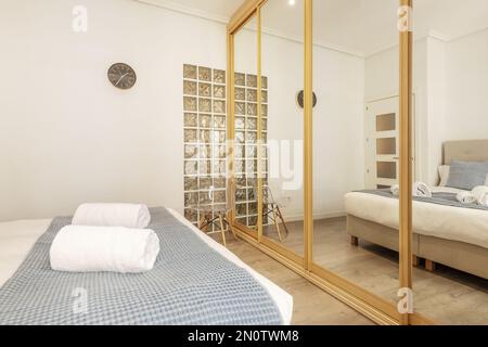 Ein Doppelzimmer mit einem großen Kleiderschrank, der eine Wand mit Spiegelschiebetüren mit Eichenholzkanten und ein Dachfenster mit Glaspflastersteinen bedeckt Stockfoto