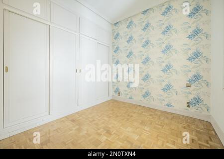 Leeres Schlafzimmer mit weißem Türschrank im venezianischen Holzstil an einer Wand, Wände mit blau gemusterter Tapete und heller Eichenparkettfußboden Stockfoto