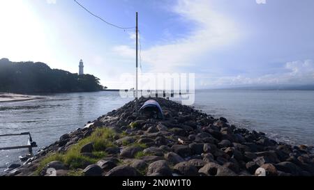 Die Felsen an der Küste werden in eine Straße zwischen dem Meer und dem Fluss, dem Hafen, dem Strand und dem Himmelblau gestapelt Stockfoto