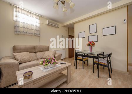 Ein Wohnzimmer mit beigefarbenem Sofa, quadratischem schwarzem Holz und Glasesstisch und passenden Stühlen Stockfoto