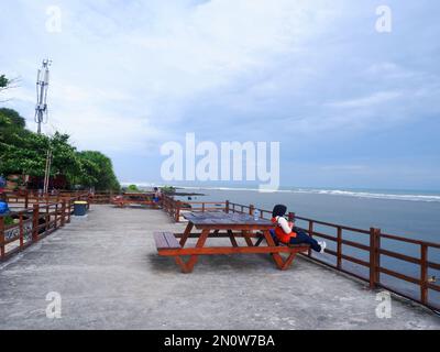 Garut, Indonesien - Dezember 12,2022: Die Person, die auf der hölzernen Strandbank auf der Küstenbrücke der tropischen Insel saß. Ein entspannender urlaub Stockfoto