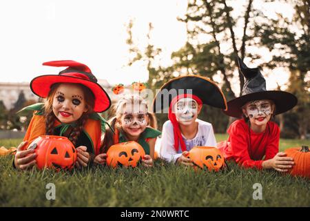 Süße kleine Kinder mit Eimern für Kürbisbonbons in Halloween-Kostümen im Park Stockfoto