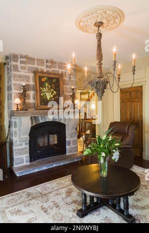 Grauer Natursteinkamin und runder hölzerner Couchtisch im Wohnzimmer im Haus im Renaissance-Stil. Stockfoto