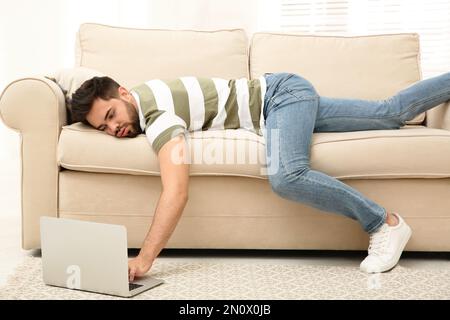 Fauler junger Mann, der zu Hause auf dem Sofa auf dem Laptop liegt Stockfoto