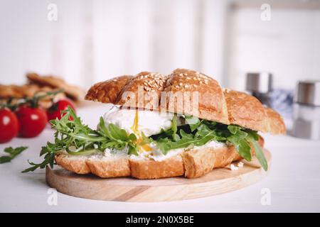 Köstliches Croissant mit Rucola und Ei auf weißem Holztisch, Nahaufnahme Stockfoto