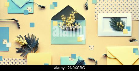 Mimosablüten, mintgrüne Umschläge und Farbpapier auf gelbem goldenem Hintergrund. Knolling, ordentlich gestaltete Einrichtung im Frühling. Flach liegend, Draufsicht. Stockfoto