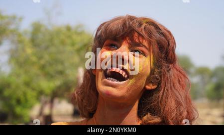 Hübsches junges Mädchen, das mit explodierendem rosa-gelbem Holi-Pulver um sich herum posiert