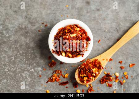 Blick von oben auf Chili-Flocken mit rotem heißem Pfeffer in weißer Schüssel und Holzlöffel Stockfoto