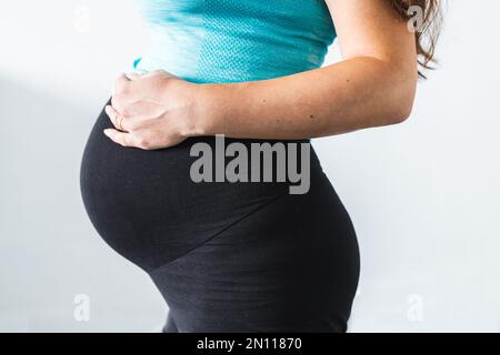 Schwangere Frau berührt ihren Bauch im letzten Stadium der Schwangerschaft, in der Mitte des Abschnitts zeigt sich Bauch und Körperform, trägt Umstandsshorts Stockfoto