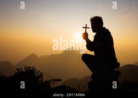Silhouette eines christlichen Mannes, der Hand betet, eines Mannes, der ein Kruzifix hält, der betet, Spiritualität und Religion, einer Frau, die zu gott betet. Das Christentum-Konzept. Stockfoto